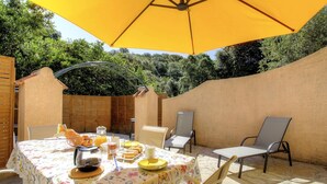 Eine Terrasse im Freien mit einem für das Frühstück gedeckten Tisch, umgeben von Stühlen und einem gelben Sonnenschirm.