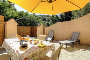 An outdoor patio with a table set for breakfast, surrounded by chairs and a yellow umbrella. - L'Orangeraie 3 - SAGONE (SAGONE)