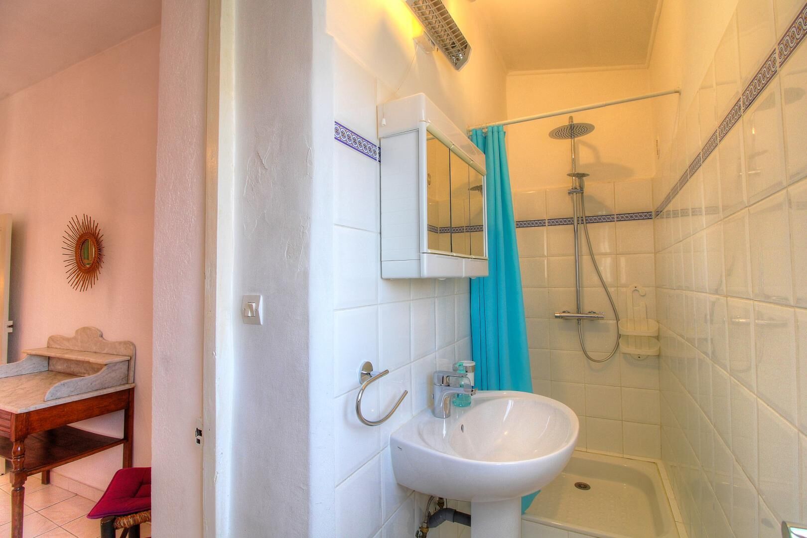 Un baño con lavamanos blanco, un espejo, ducha con cabezal de ducha manual y una bañera.
