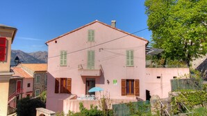 Un bâtiment rose avec des volets verts, un escalier et une table avec des chaises à l’extérieur.