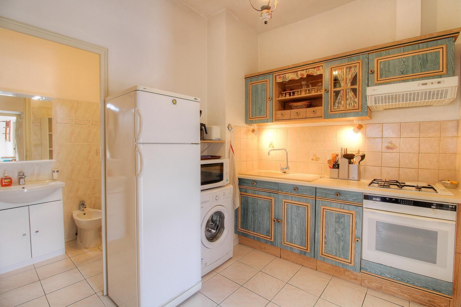 Eine Küche mit Kühlschrank, Waschmaschine, Backofen, Spüle und Schränken.