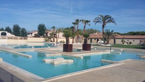 A swimming pool with multiple lanes, palm trees, and a clear blue sky. - Nice holiday house, 3 bedrooms, AIRCO upstairs, a secured residence with pools,slides. Wifi, at... (PORTIRAGNES)