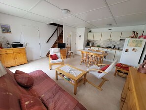 Ein kompakter Wohnbereich mit Sofa, Sesseln, einem Esstisch, einer Küchenzeile und einer Treppe.