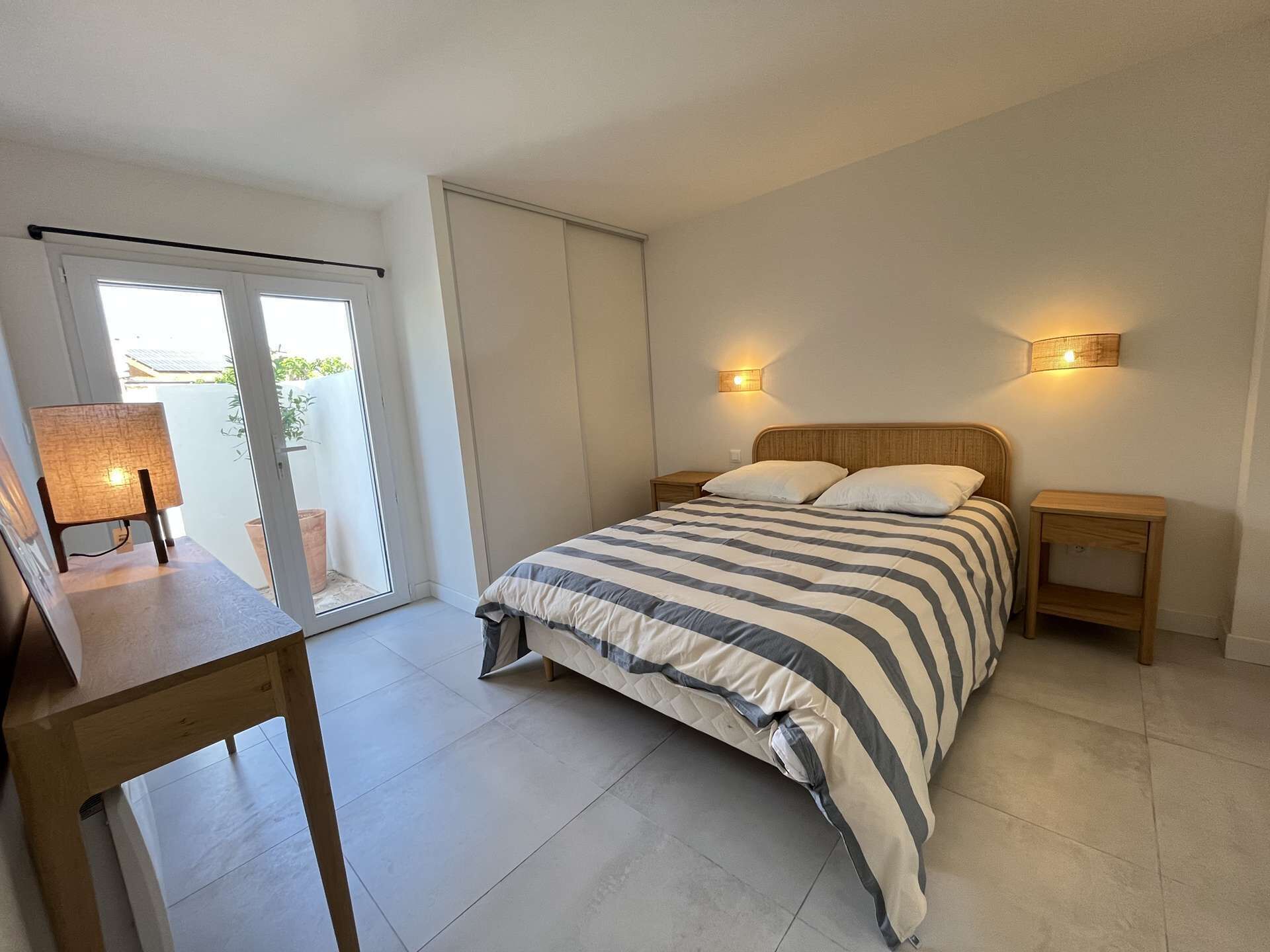 Ein Schlafzimmer mit einem Bett, Nachttischen, einem Schreibtisch und einer Schiebetür, die auf einen Balkon führt.