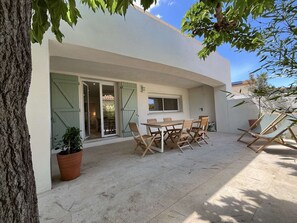 Eine Terrasse mit Tisch, Stühlen, einem Blumentopf und einem Baum.