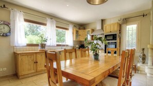 Una cocina con armarios de madera, una mesa de comedor con sillas, una planta en maceta y un reloj en la pared.