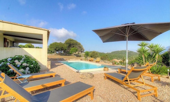 Ein Poolbereich mit Liegestühlen und einem Sonnenschirm, umgeben von Grünflächen und Hügeln.