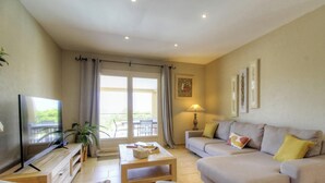 Una sala de estar con televisor, sofá, mesa de centro y puerta al balcón.