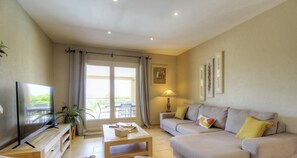 Ein Wohnzimmer mit Fernseher, Sofa, Couchtisch und Balkontür.