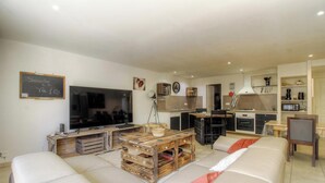 Ein Wohnzimmer mit Fernseher, Holzmöbeln, einer Couch und einer Küchenzeile mit Mikrowelle und Backofen.