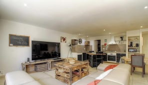 Ein Wohnzimmer mit Fernseher, Holzmöbeln, einer Couch und einer Küchenzeile mit Mikrowelle und Backofen.