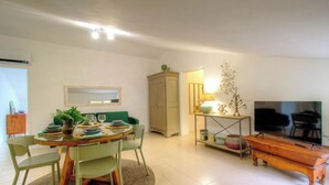 Ein Wohnzimmer mit Esstisch, Stühlen, einer Couch, einem Fernseher und einem Schrank.