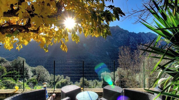 Une terrasse dotée de meubles en osier, avec une vue sur les montagnes et un ciel dégagé.