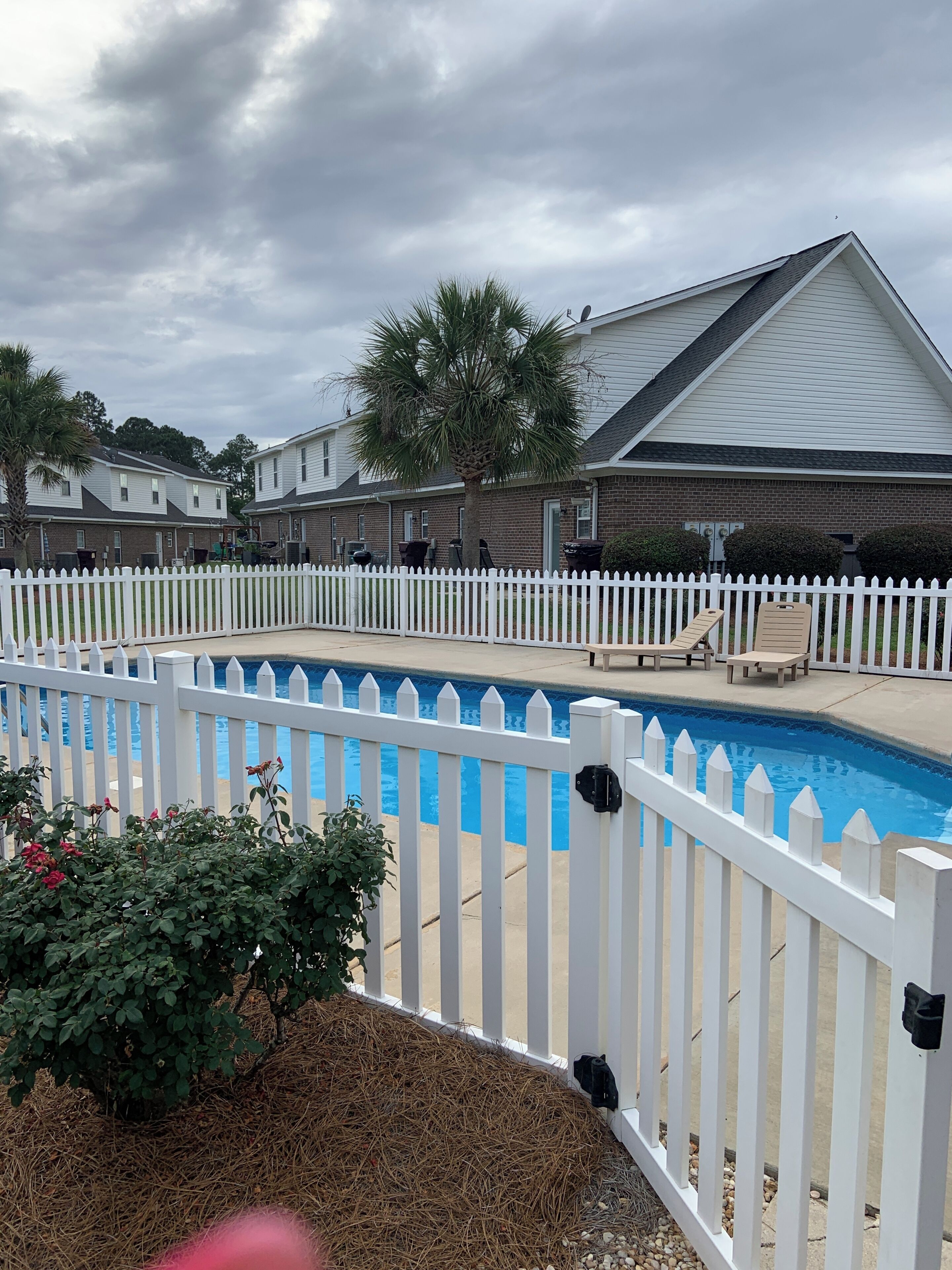 A residential area with a swimming pool, white picket fence, and houses with brick exteriors.