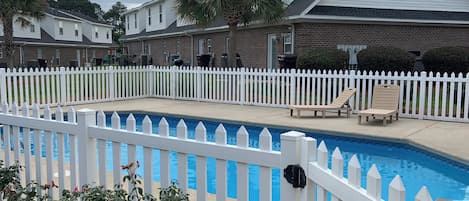 A residential area with a swimming pool, white picket fence, and houses with brick exteriors.