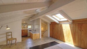 Ein Loft-Zimmer mit freiliegenden Holzbalken, einem Oberlicht, einem Holzschrank, einer kleinen Küchenzeile und einem Sessel.