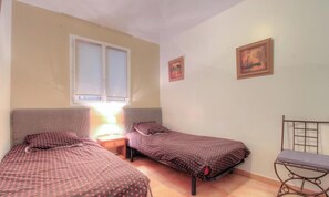 Ein Zimmer mit zwei Betten, einem Fenster, einem Sessel und zwei Bildern an der Wand.