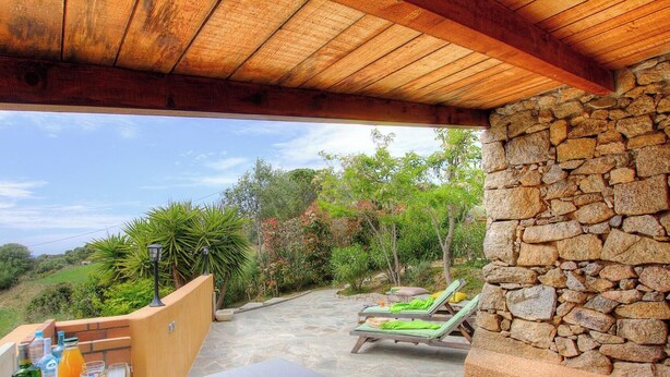 Un espacio al aire libre techado, con paredes y camino de piedra, y dos sillones de descanso.