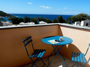 Ein Balkon mit einem blauen Tisch, zwei blauen Stühlen, einer Zeitschrift und einer Tasse.