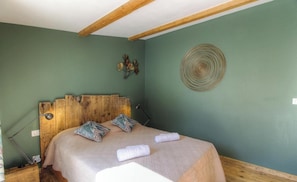 Ein Schlafzimmer mit einem Holzkopfende, einem Bett mit blumigen Kissen, einer Wanddekoration und einer Nachttischlampe.