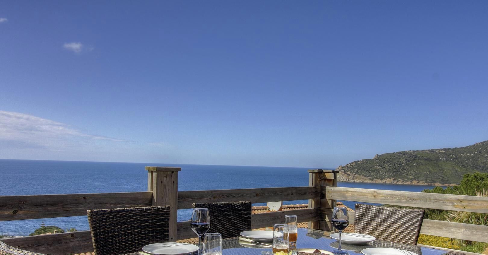 A table set for two with a view of the sea and a wooden deck.