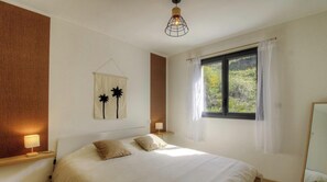 Ein Schlafzimmer mit einem Bett, Nachttischlampen, einem Wandbild, einem Fenster mit Vorhängen und einer Pendelleuchte.