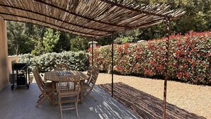 Eine Terrasse im Freien mit Tisch und Stühlen, umgeben von einem Garten mit roten Blättern und einer darüberliegenden Pergola.