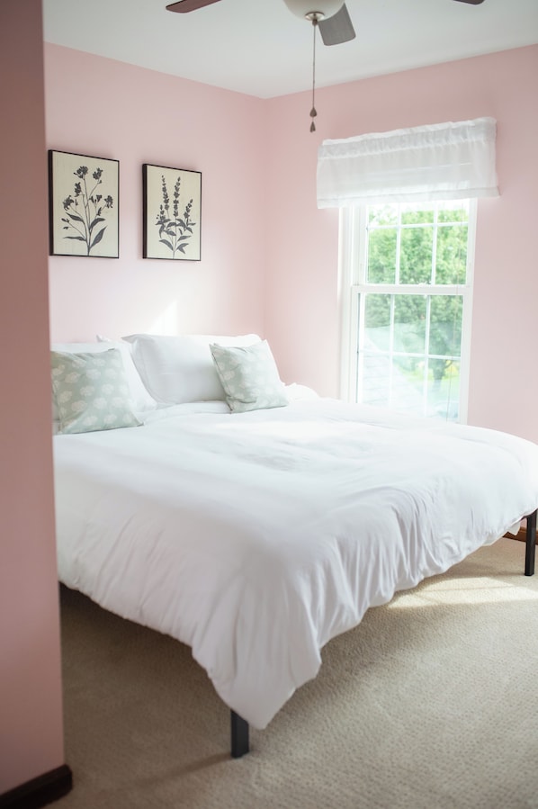 A bedroom with a bed, a window with a white valance, and two wall-mounted floral artwork.