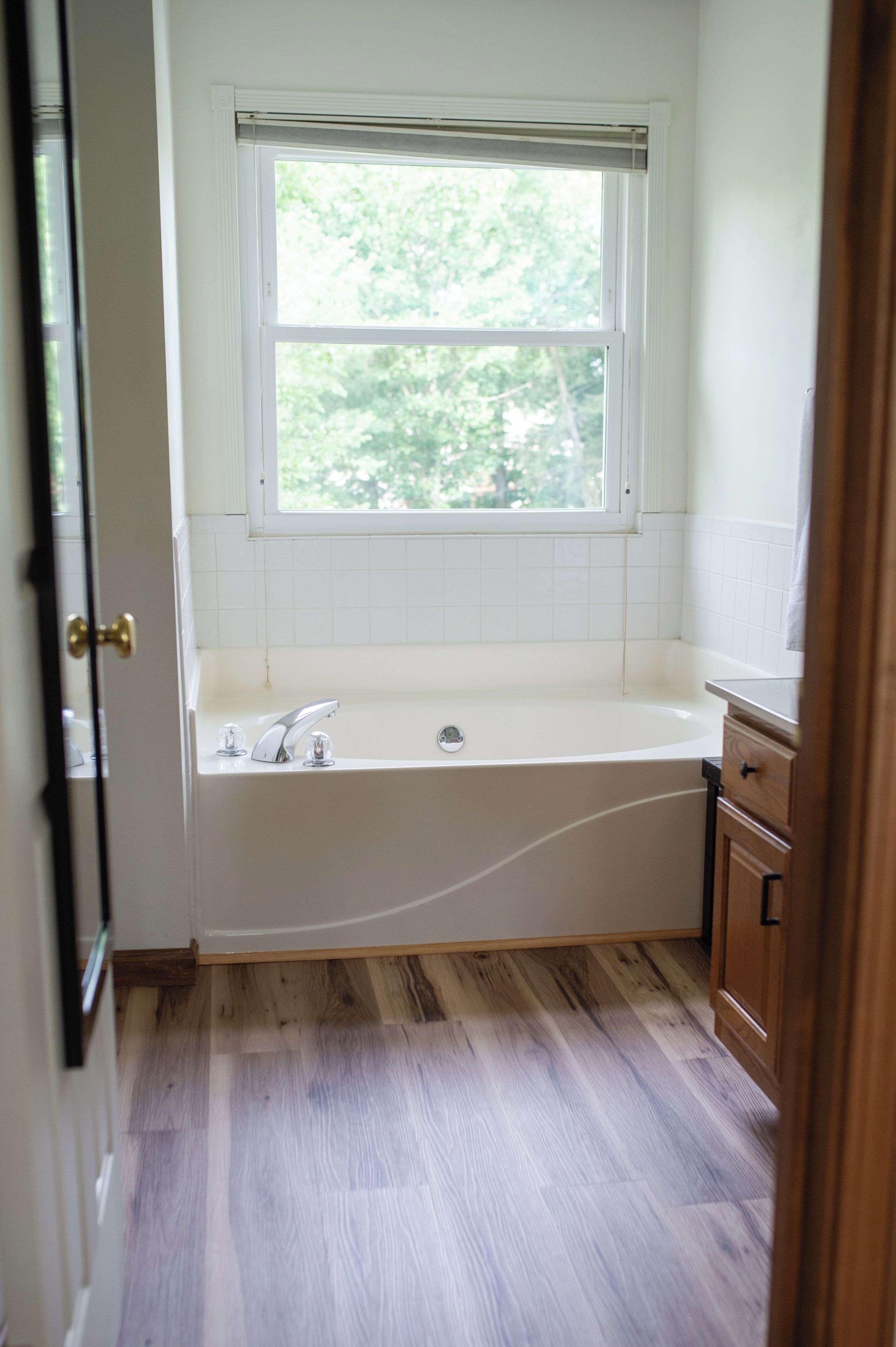 A bathroom with a window, a bathtub, a sink, and wooden flooring.