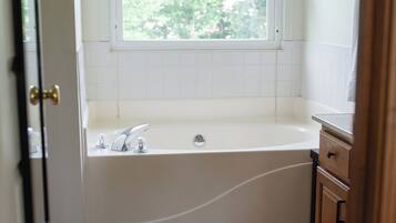 A bathroom with a window, a bathtub, a sink, and wooden flooring.