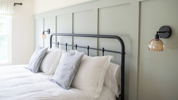 A bed with a metal headboard, multiple pillows, and a wall-mounted light fixture. - Large Family Home with Backyard Oasis & Fire Pit (Florence)