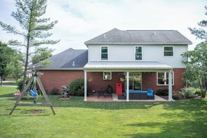 A two-story house with a covered patio, a swing set, and a red door.
