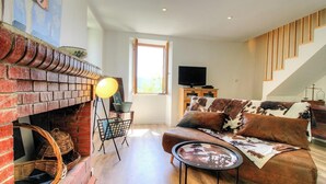 Ein Wohnzimmer mit Kamin, Sofa, Fernseher und einer Treppe.