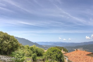 Eine gebirgige Landschaft mit blauem Himmel, einem Gewässer in der Ferne und einem Gebäude mit roten Ziegeln.