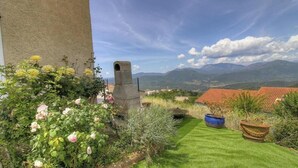 Un balcón con vista a montañas, una chimenea de piedra y plantas en macetas.