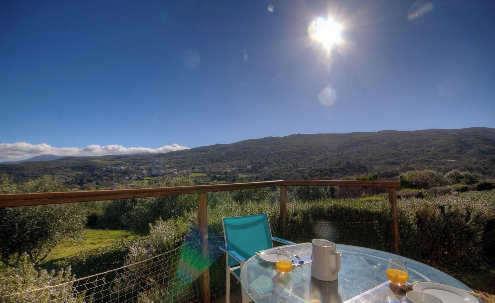 Ein Esstisch mit Glasplatte, ein Stuhl, ein Teller, ein Glas Orangensaft und eine Tasse, vor einer malerischen Aussicht auf Hügel und klaren Himmel.