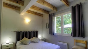 Ein Schlafzimmer mit einem Bett, zwei Nachttischlampen, einem Fenster mit Vorhängen und einer Holzbalkendecke.