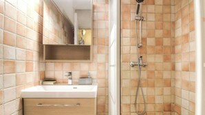 A bathroom with a white sink, a mirror, a shower with a handheld showerhead, and tiled walls. - Les chênes verts 2 - CONCA (CONCA)