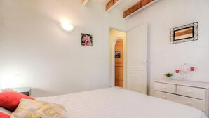 A bedroom with a bed, a dresser, a nightstand, a wall-mounted light, and a door leading to another room. - Les chênes verts 2 - CONCA (CONCA)