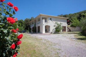 Ein zweistöckiges Gebäude mit einem Balkon, einer Schotterauffahrt und einem Garten mit roten Rosen.