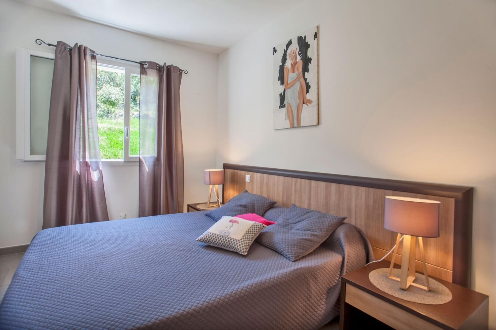 Un dormitorio con una cama, dos mesitas de noche con lámparas, una ventana con cortinas y un cuadro en la pared.