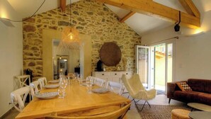 A dining area with a wooden table set for six, stone walls, a hanging light fixture, and a sofa in the foreground. - Cuccia - CORSCIA - Guest house (CORSCIA)