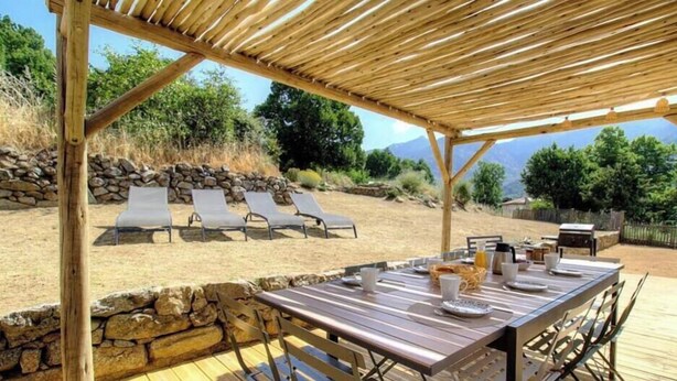 A covered outdoor dining area with a stone wall and lounge chairs in the background. - Cuccia - CORSCIA - Guest house (CORSCIA)