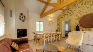 A cozy living room with a fireplace, a dining area with a table and chairs, and a stone wall. - Cuccia - CORSCIA - Guest house (CORSCIA)
