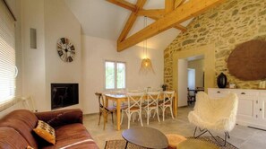 Un salon chaleureux avec une cheminée, un coin repas avec une table et des chaises, et un mur en pierre.