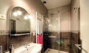 Un bany modern amb un box de dutxa de vidre, un mirall gran i un lavabo blanc.