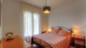 A bedroom with a bed, a table with a plant, a window with curtains, and a hanging light fixture. - I dui cipressi - BASTELICACCIA (BASTELICACCIA)