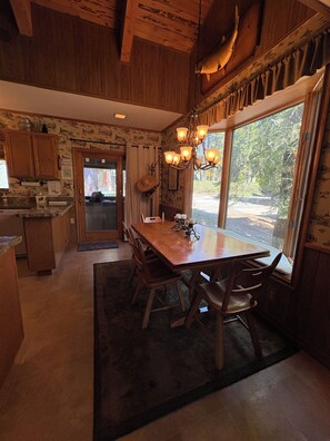 A wooden interior with a dining table, chairs, a chandelier, and a view through large windows. - Largest Townhome in Leland Meadows, Plus a Hot Tub! (Pinecrest)