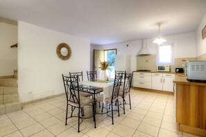 Comedor con mesa de vidrio y sillas de metal, cocina con armarios blancos y estufa, y escalera que conduce a otro nivel.