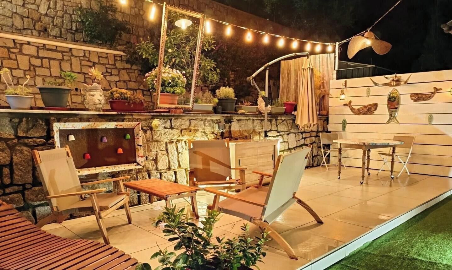 Un patio al aire libre con paredes de piedra, muebles de madera y luces de cadena.